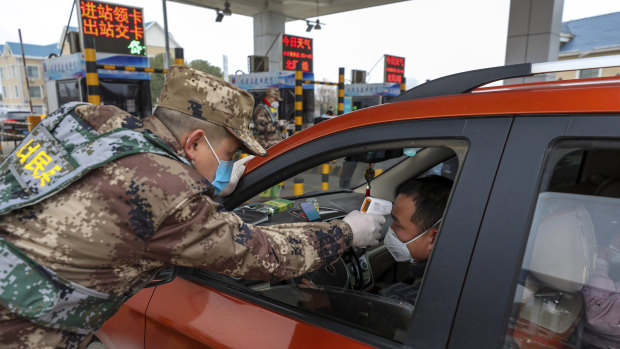 A militia member takes a driver's temperature at a checkpoint at a highway toll gate in Wuhan.
