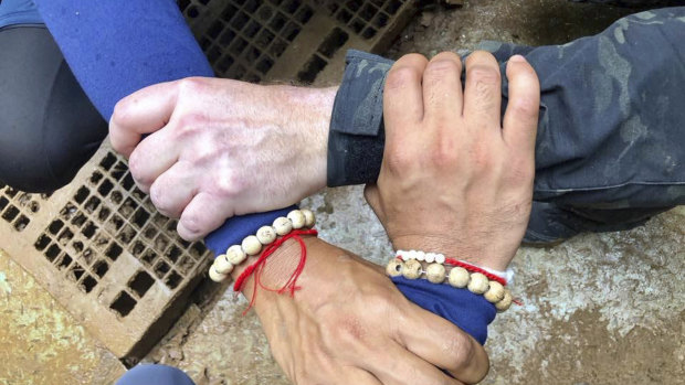 Three hands interlocked showing solidarity between Thai and international rescue workers.