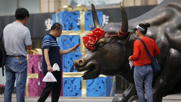 A man touches a bull statue as a couple preparing to take a picture outside a retail and wholesale clothing mall in Beijing on Monday.