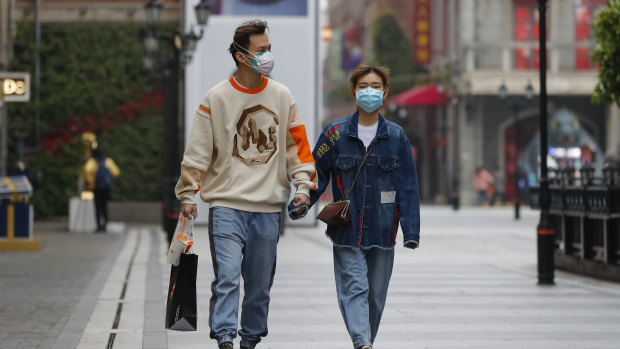 A couple wearing protective masks to prevent the new coronavirus outbreak walk on a re-opened commercial street in Wuhan.