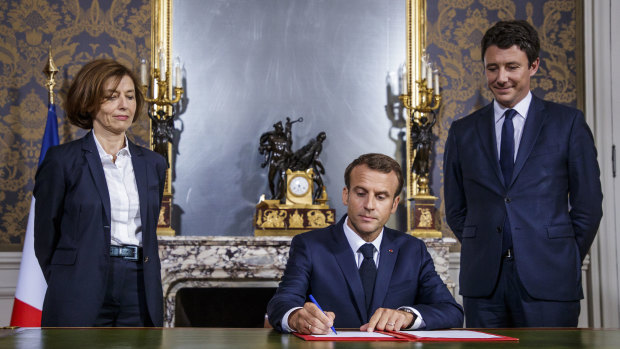 French President Emmanuel Macron, center, flanked by French Defence Minister Florence Parly, left, and French government spokesman Benjamin Griveaux, signs the armed forces annual law budget, at the Hotel de Brienne, in Paris in July.