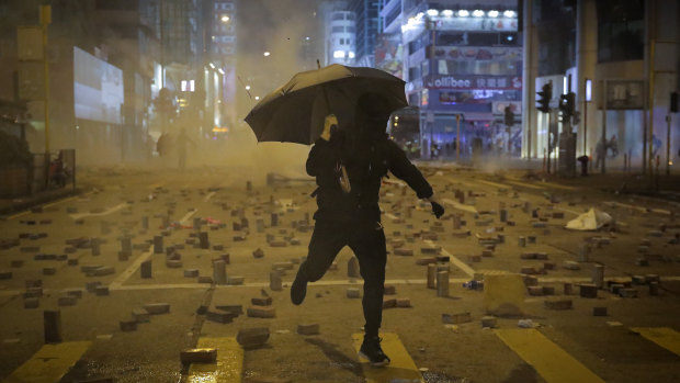 A protester with an umbrella runs away from tear gas fired by riot police on a street scattered with bricks during a protest in Hong Kong late last year.