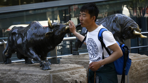 A man touches a bull statue outside a bank in Beijing. Chinese shares tumbled after President Donald Trump tweeted a threat to raise more tariffs on imports from China, spooking investors who had been expecting good news this week.