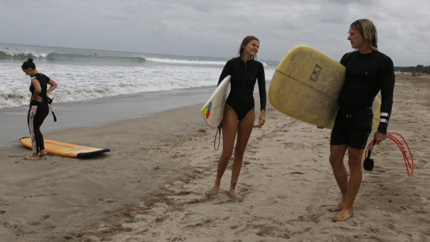 Foreign tourists carry their surf board at Kuta beach, Bali, after a three-month virus lockdown lifted, allowing local people and stranded foreign tourists to resume public activities before foreign arrivals resume in September.