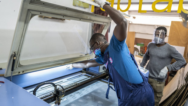 Mohamed Gueye, centre, and Idrissa Sall, right, use a laser cutter to make protective face shields.