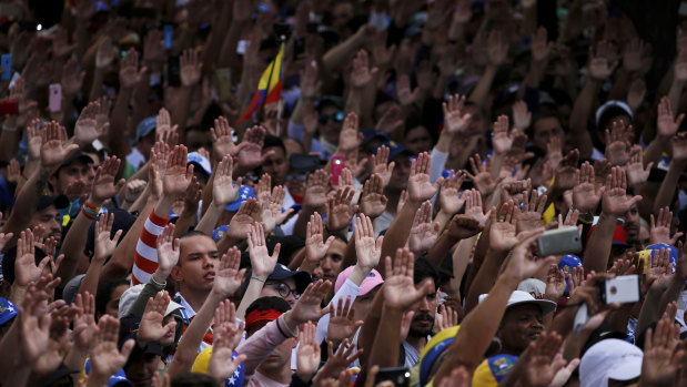 Anti-government protesters hold their hands up during the symbolic swearing-in of Juan Guaido in Caracas on Wednesday.