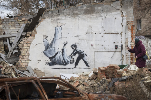 A woman takes a picture of an artwork on a building in Borodyanka, Kyiv region. The artwork was supposedly made by British street artist Banksy.