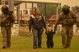 Two Australian Army soldiers help people evacuate onto a Chinook helicopter at Omeo showgrounds in Victoria on Sunday.