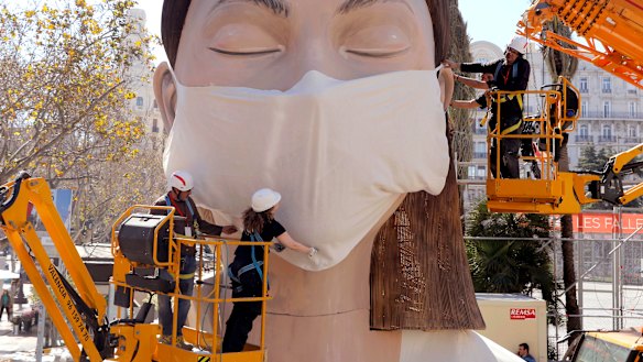 Workers place a mask on the figure of the Fallas festival in Valencia – the festival was cancelled because of the pandemic.