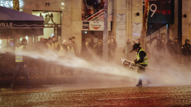 A demonstrator wearing a yellow vest is blasted with a police water canon on the Champs-Elysees in Paris on Saturday.
