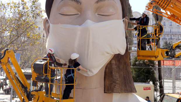 Workers place a mask on the figure of the Fallas festival in Valencia – the festival was cancelled because of the pandemic.