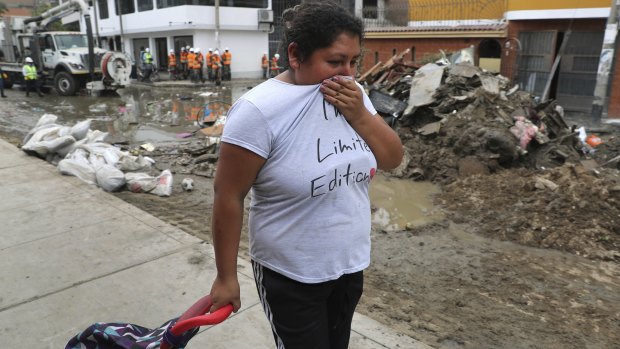 A woman covers her nose as she passes a street flooded with sewage water in Lima's San Juan de Lurigancho district.