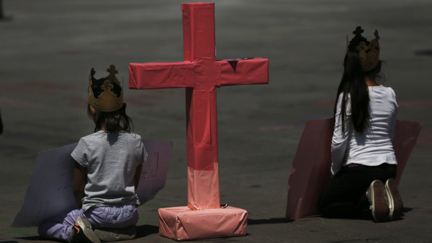 Girls sit next to a cross to remember murdered women in Mexico City, during the national "A day without women" strike on Monday.