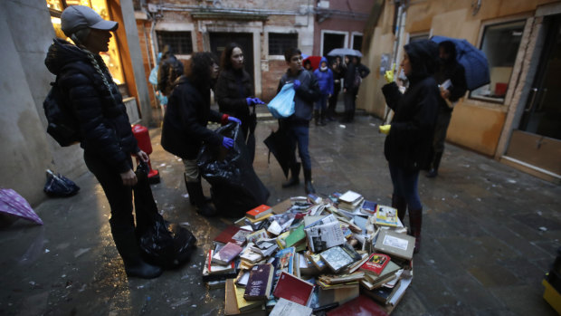 Young volunteers help the clean up, throwing out damaged books from renowned bookstore "Acqua Alta" in Venice.