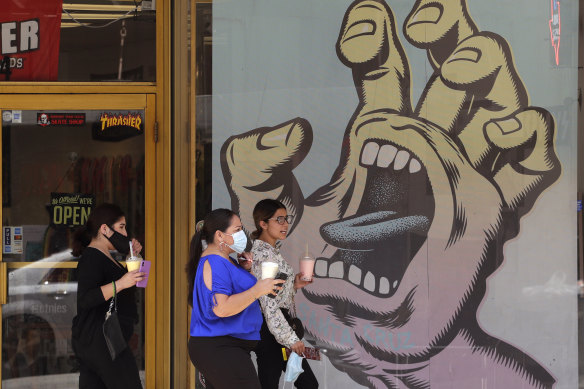 People wearing masks to protect against the spread of COVID-19 pass a mural on a business that has reopened in San Antonio, Texas, where cases of COVID-19 have spiked.