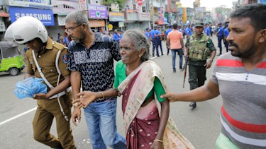 Sri Lankan elderly woman is helped near St. Anthony's Shrine after a blast in Colombo, Sri Lanka.