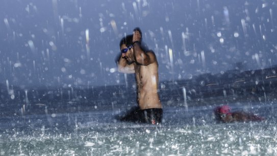 A swimmer braves the water at Bondi Beach as a downpour sweeps across the beach on Thursday morning.
