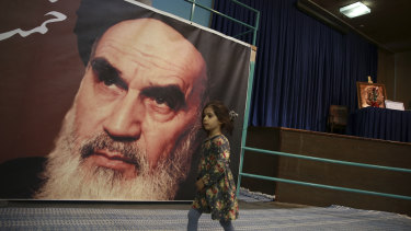 A girl walks past a poster of Ayatollah Ruhollah Khomeini, at a mosque where he made speeches, in northern Tehran, Iran. The memory of Khomeini, who died in 1989 at the age of 86, looms large over Tehran.