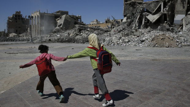 Syrian students run in front of buildings that were destroyed last summer during fighting between US-backed Syrian Democratic Forces fighters and Islamic State militants, in Raqqa, Syria. 