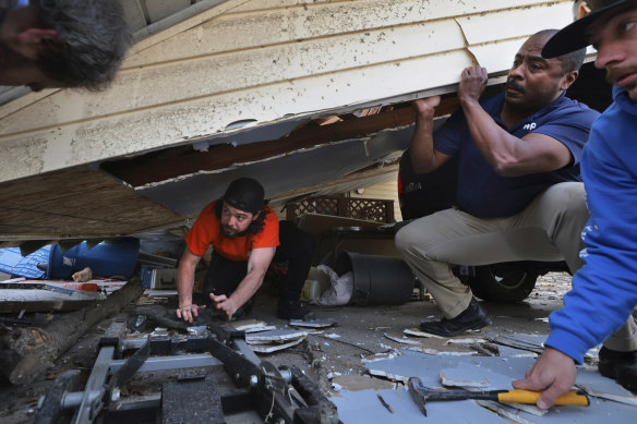 Matt Wolff, left, works underneath his carport with the help of his father-in-law Dempsey Watson and friend Tyler Umbright, right, as they work to stabilize after a severe storm in Bridgeton, Mo.