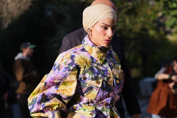 A guest wears a beige headscarf, gold earrings, a purple / green / yellow floral print pattern cotton puffy sleeves / high neck / belted oversized jacket, matching purple / yellow / green floral print pattern flared suit pants, a yellow leather Birkin handbag from Hermes, outside Zimmermann, during Paris Fashion Week - Womenswear Fall/Winter 2026/2027, on March 09, 2026 in Paris, France (Photo by Edward Berthelot/Getty Images)