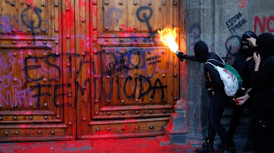 A masked, female protester sprays fire at the entrance to the National Palace in Mexico City.
