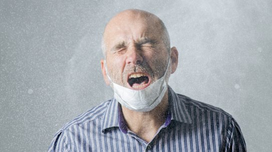 Man sneezing with spray of water droplet full of virus or microbes
He wears his face mask inappropriately on his chin Sneeze droplets virus contagious