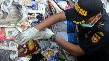 Indonesian Customs official Dhion Priharyanto holds up a used nappy, soft drink containers and a plastic of organic raspberries mixed in with paper that was supposed to be recycled. Instead, it will be sent back to Australia. 