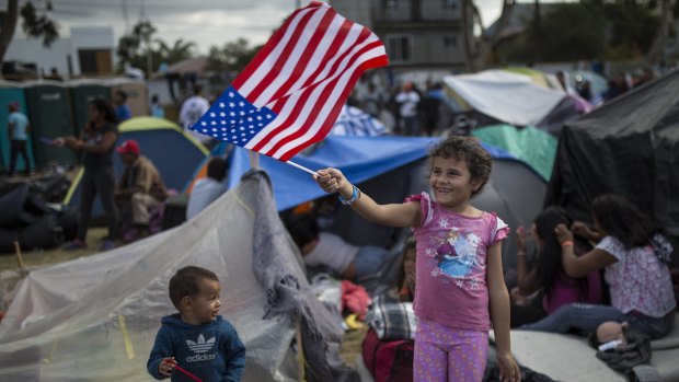 Seven-year-old Honduran migrant Genesis Belen Mejia Flores waves an American flag at US border control helicopters flying overhead near the Benito Juarez Sports Centre serving as a temporary shelter for Central American migrants, in Tijuana, Mexico, on Saturday.