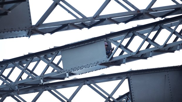 A man sits in a box in the framework of the Sydney Harbour Bridge as police negotiate with him. He was arrested shortly before 10am.