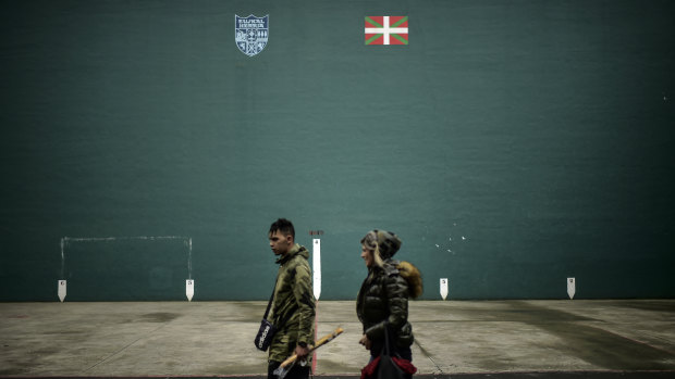 A couple walk past beside a wall painted with the Basque flag, or Ikurrina, top right, and the symbol of the Basque Country, in the small in the small basque village of Hernani, northern Spain.