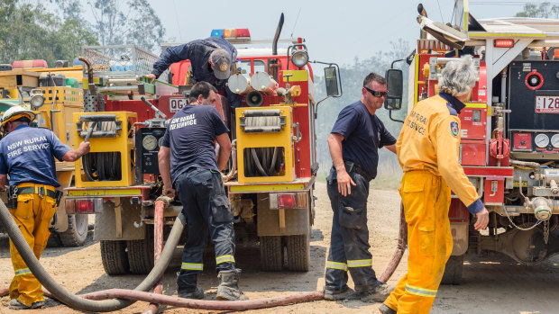 Captain Creek and Queanbeyan City rural firefighters refill their fire trucks at Captain Creek, Queensland, on Sunday.