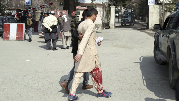 An injured man is assisted to hospital after three explosions struck a Shiite shrine in Kabul. 