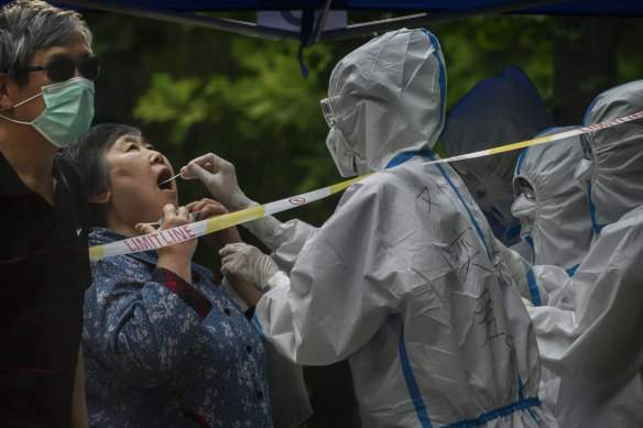 A Chinese epidemic control worker wears a protective suit and mask while performing a nucleic acid test for COVID-19 on a woman at a testing center in Beijing.