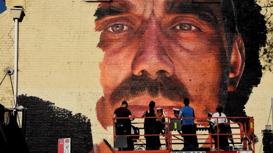 A group of artists paint a mural of Adam Goodes on the wall of a building on the corner of Foveaux street and Crown street in Surry Hills.
