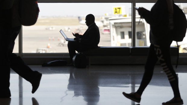 A traveller pauses to check his phone and computer as he waits for his flight at Indianapolis International Airport in Indianapolis.
