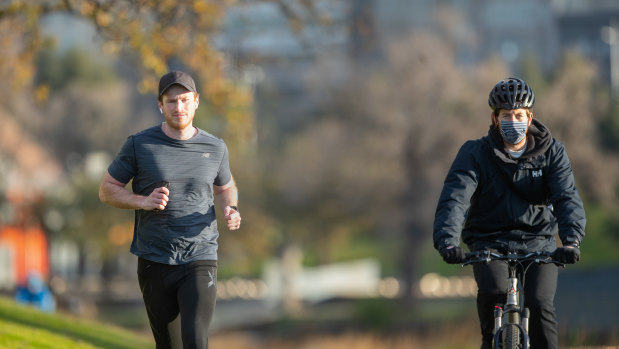 Jogger Marshall Pascoe (left) runs past a masked cyclist along the Yarra River in Melbourne on Saturday morning. 