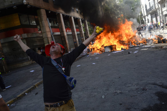 A demonstrator protests in front of a burning barricade.