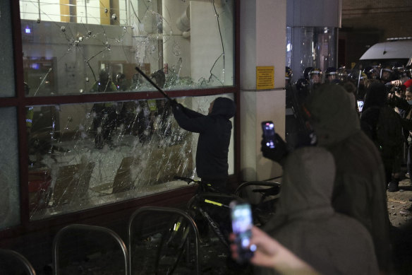 A protester smashes a window with a stick outside Bridewell Police Station, in Bristol.