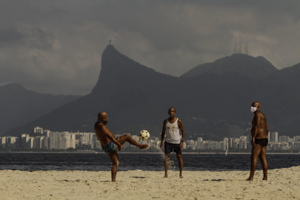People play football on a Niteroi beach, with Rio de Janeiro and its Christ the Redeemer statue in the background. Despite the proximity, the two cities have very different rates of dengue.