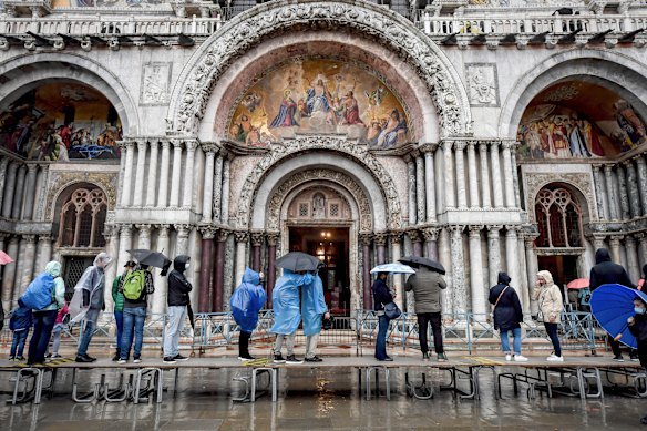Visitors stand on a trestle bridge as they admire St. Mark's Basilica during an expected high water, in Venice, northern Italy, on Saturday.