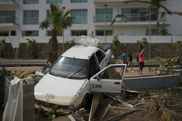 A damaged car lies on a street split by Otis in Acapulco. The hurricane that strengthened swiftly before slamming into the coast as a category 5 storm has killed at least 27 people as it devastated the resort city.