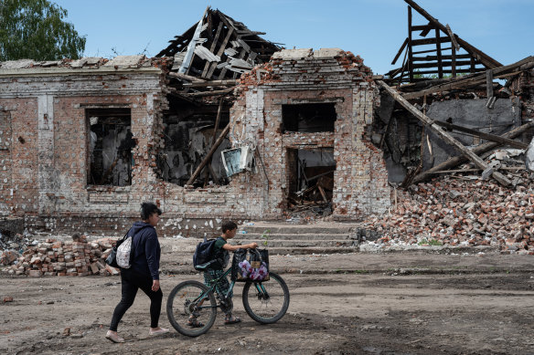 A woman and a boy with a bike walk by destroyed buildings in Trostyanets, Ukraine, on Thursday.