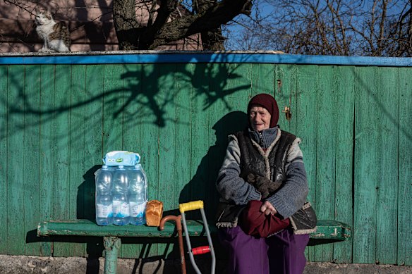 Liubov sits on the bench by her house while her cat sits on the fence in Andriivka, Ukraine.