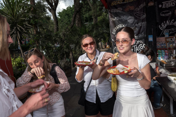 Kate Paliotta, Catherine Verklin and Cecelia Galligan, visitors from New York, eat tacos at a street stand in the Roma Norte neighbourhood of Mexico City.