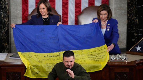 US House Speaker Nancy Pelosi and Vice President Kamala Harris, left, hold open a Ukrainian flag that was presented to them by Ukrainian President Volodymyr Zelensky.