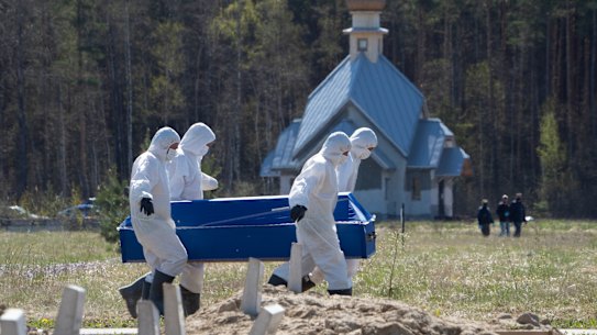 Grave diggers wearing personal protective suits carry a coffin while burying a COVID-19 victim in the special purpose for coronavirus victims section of a cemetery in Kolpino, outside St.Petersburg, Russia, Sunday, May 10, 2020. 