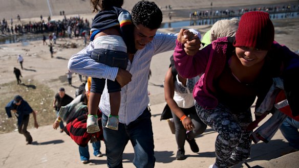 Migrants walk up a riverbank at the Mexico-US border after getting past a line of Mexican police.