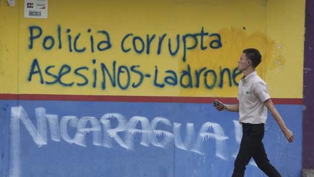 A man walks past graffiti that reads in Spanish "Corrupt police. Murderers-Thieves" in Managua.