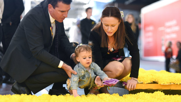 Tim and Tegan lay a commemorative flower with their two-year-old daughter Lexie.
